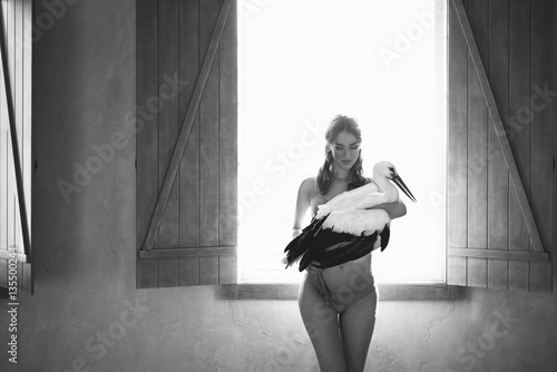 Fotografia Pregnant woman with a stork on the hands near the window in black and white styl