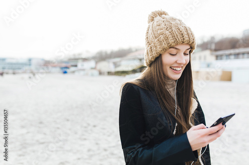 Close up portrait of a young woman in beach with phone. She is writing message and listeting music with charming smile. photo