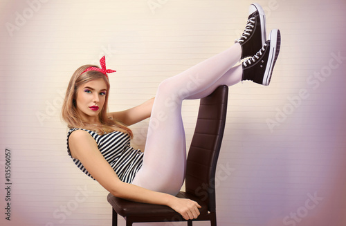 Woman in white tights and sneakers sitting on chair against color wall background