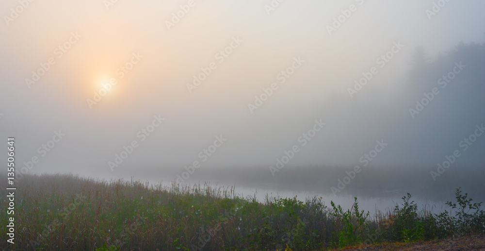 Brilliant & bright mid-summer sunrise on a narrow passage of a lake.   Warm water & cooler air at daybreak create local misty fog. 