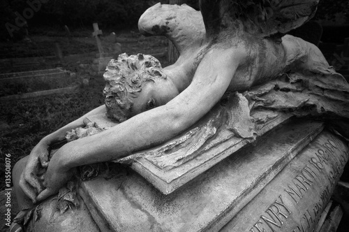 Statue of a weeping angel laying over an ancient grave