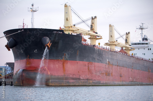 Large commercial ship sits at dock while pumping water out of a port