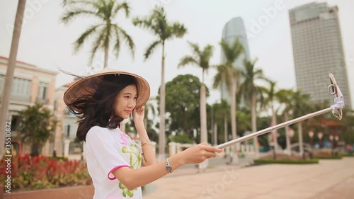 Girl in national dress makes selfie in the center of Da Nang city on the background of skyscrapers. photo