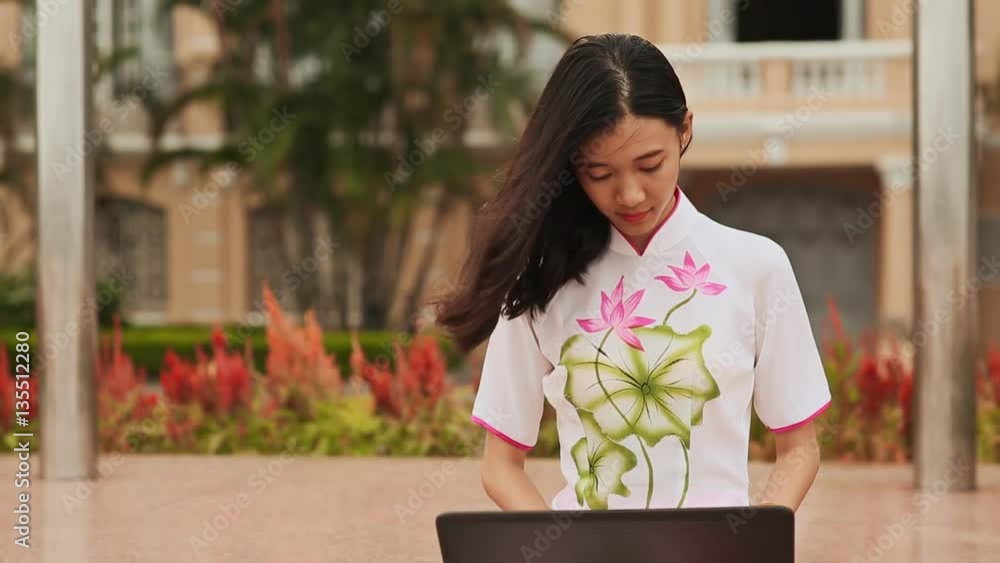Pretty Asian girl sitting with a laptop in the park in national dress ...