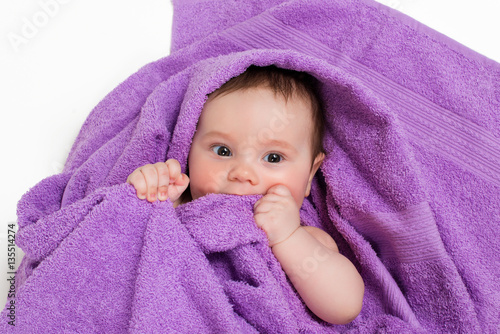 Newborn baby lying down and smiling in a purple towel