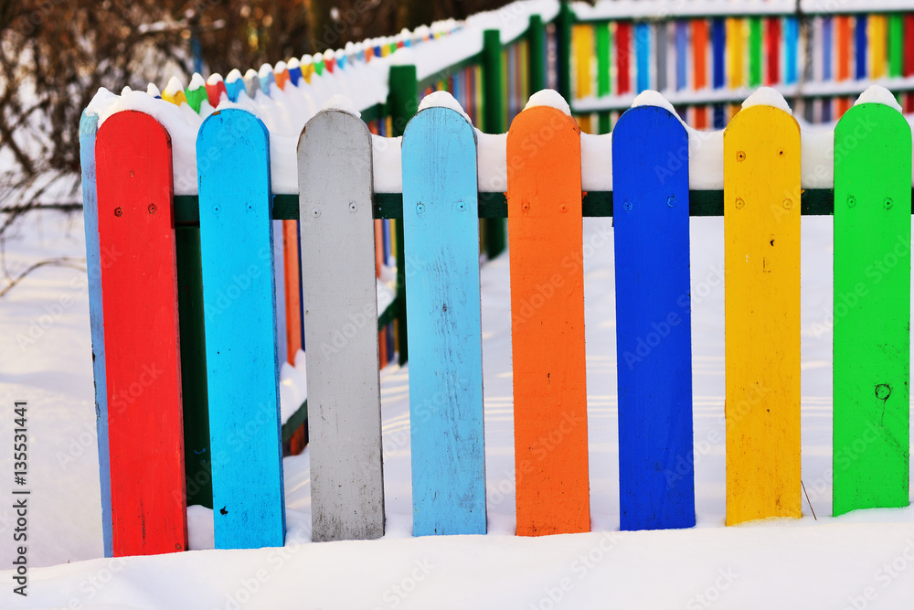 Part of Colourful vertical wooden fence painted in red, blue, green, orange, yellow and gray colors under snonw Part of Colourful vertical wooden fence painted in red, blue, green, orange, yellow and gray colors under snonw