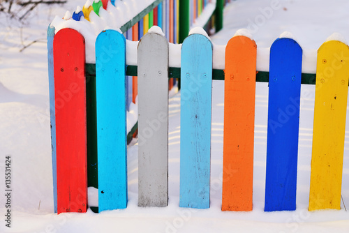 Part of Colourful vertical wooden fence painted in red, blue, green, orange, yellow and gray colors under snonw