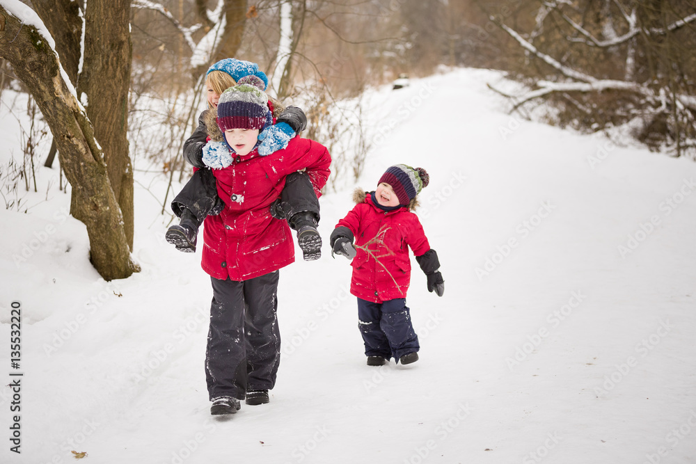 Children having fun while walking in a winter forest. Cute kid boy carrying his friend and an adorable little toddler running near by.Smiling children outdoors.