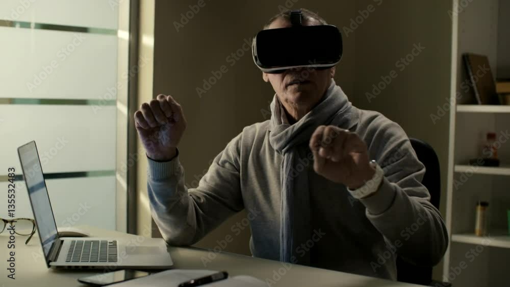 Elderly man in casual clothes wearing a virtual reality headset VR glasses and training to use cyberspace interface Elderly man in casual clothes wearing a virtual reality headset VR glasses and training to use cyberspace interface