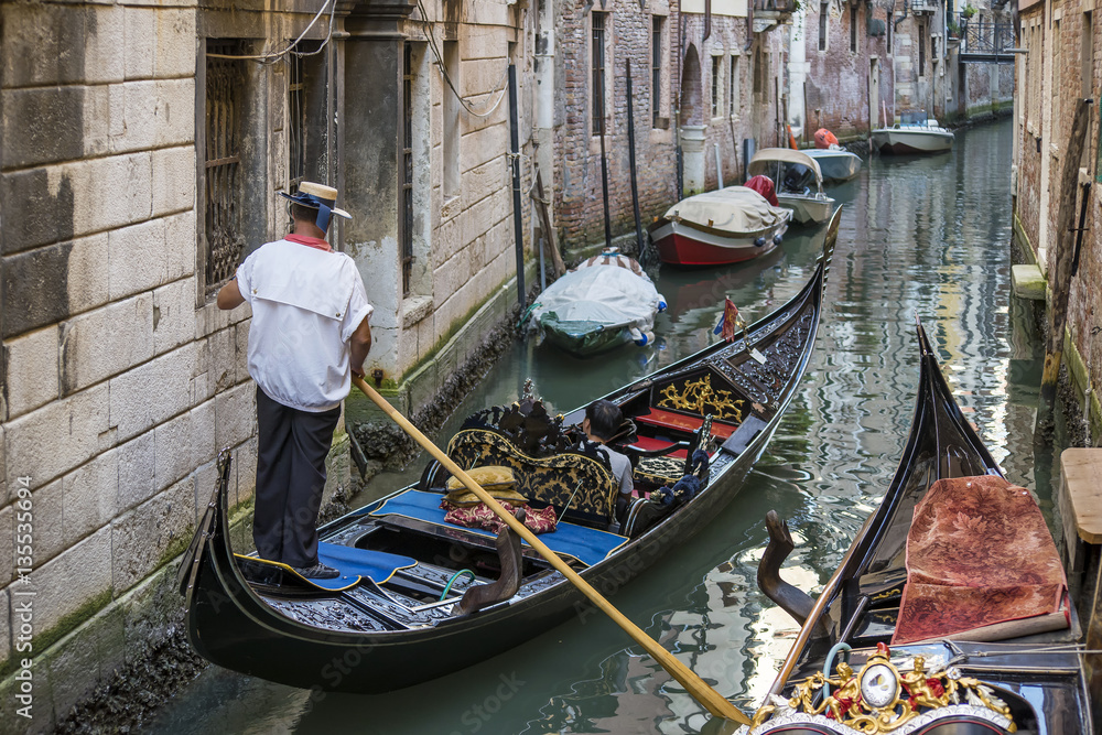 Typical gondola with standing gondolier in a narrow canal, Venice, Italy