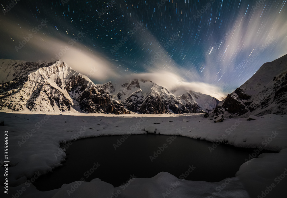 Amazing night landsape with snow peaks, star trails and small lake foreground