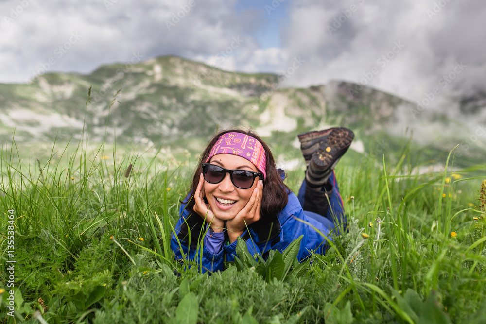 Naklejka premium Young woman relaxing on grass at high alpine meadows on hiking day