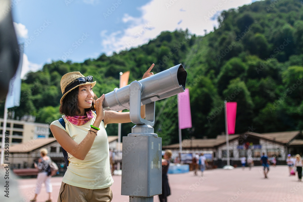 Caucasian young happy woman traveler looking into the telescope outside in the city