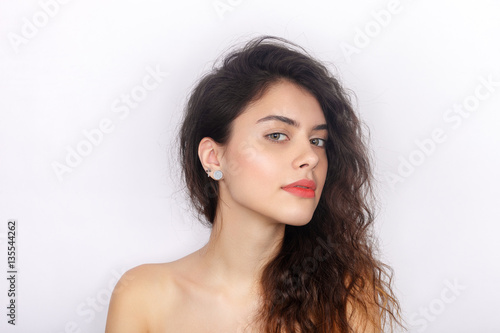 Beauty portrait of young adorable fresh looking brunette woman with healthy curly hair inquiring looks into camera. Emotion and facial expression concept.