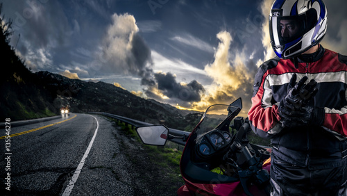 Fotografia Male motorcyclist wearing protective leather racing suit with a red bike or motorcycle on an open road