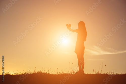 hands forming a heart shape with sunset silhouette