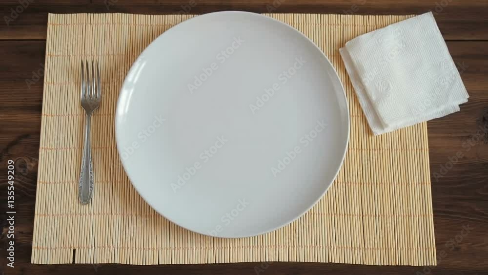 Time-lapse with old wooden table, white porcelain dish, bamboo napkin, metal fork and slices of bread. Time-lapse with old wooden table, white porcelain dish, bamboo napkin, metal fork and slices of bread.
