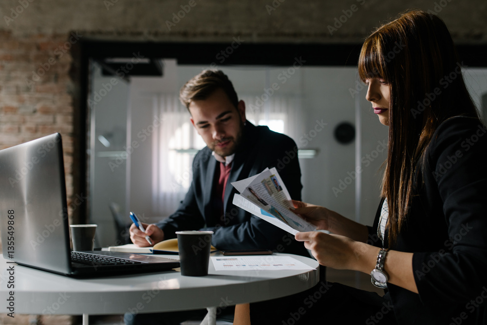 Fototapeta premium Two young people at the office sitting at the table and doing their work