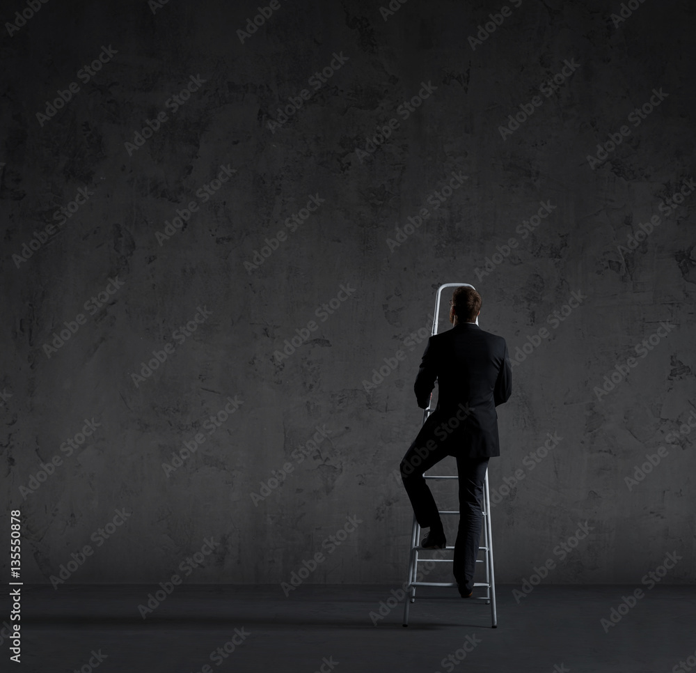 Businessman writing imaginary text on stairs. Black background w
