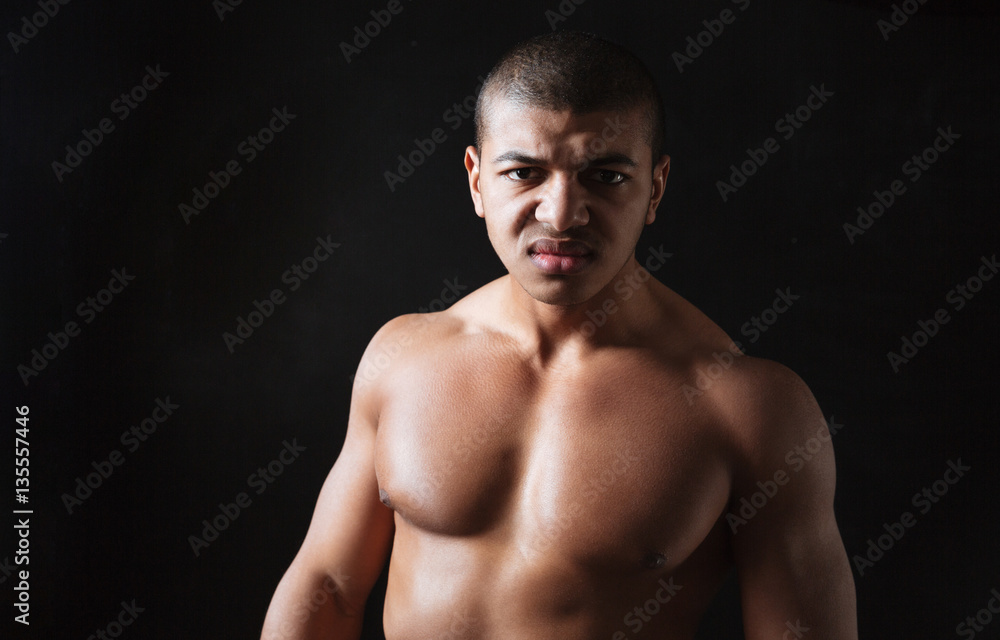 Angry young african sportsman standing over black background