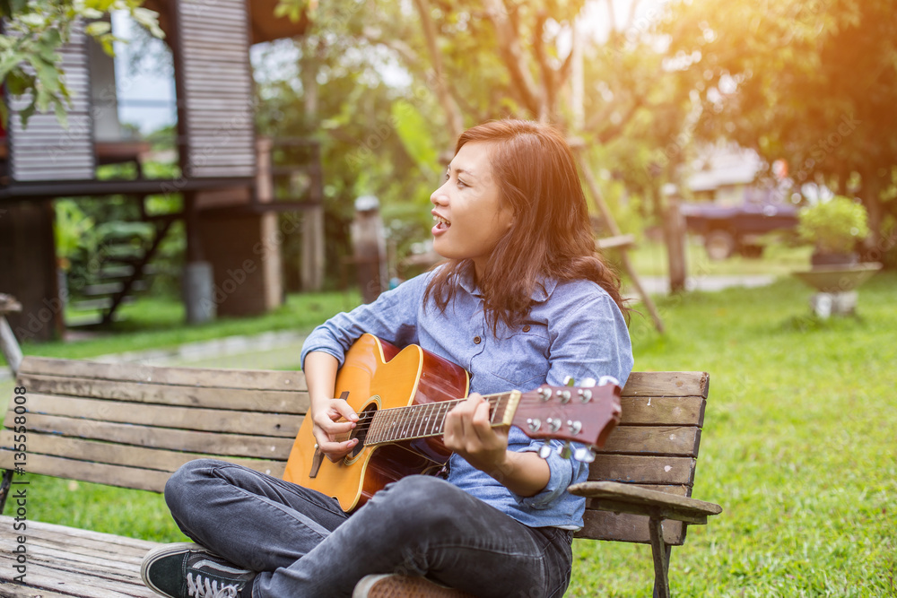 Obraz premium Beautiful young woman playing guitar sitting on bench, Happy tim