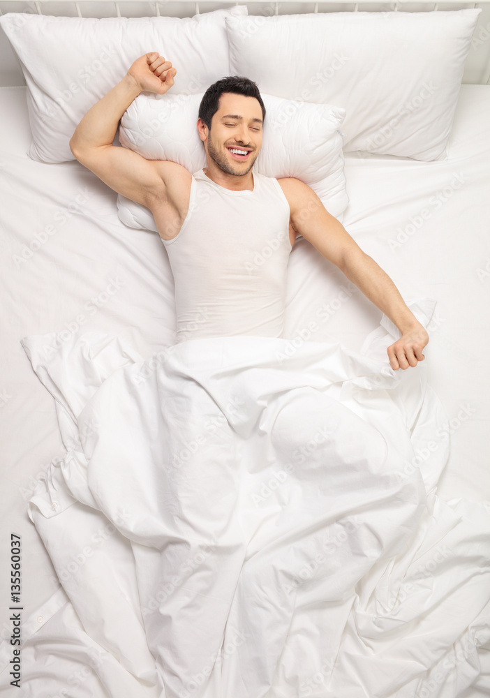 Young man lying in bed and stretching himself Young man lying in bed and stretching himself