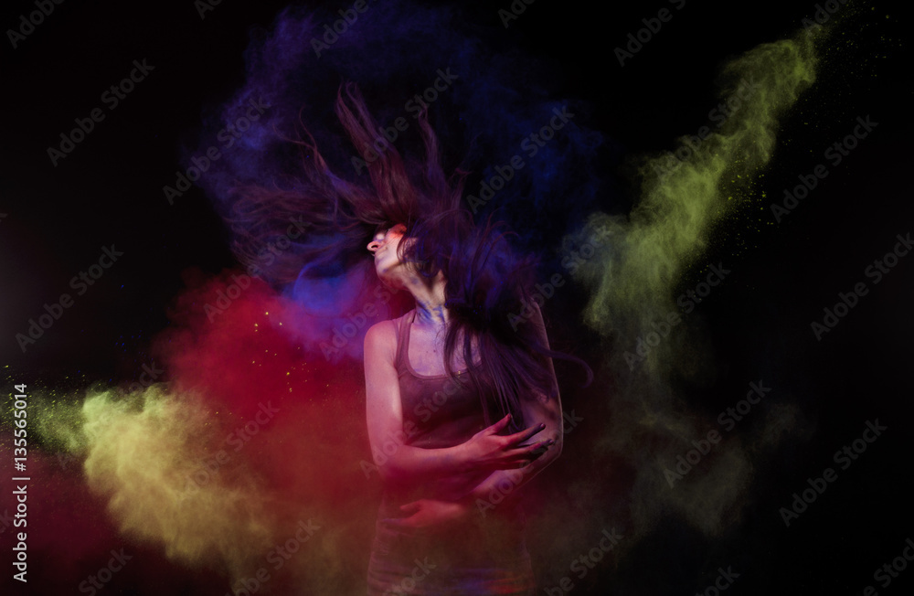 Studio photo of a young girl who throws the yellow and blue powder paint in hand and leaves a red mark paint using hair with studio light.