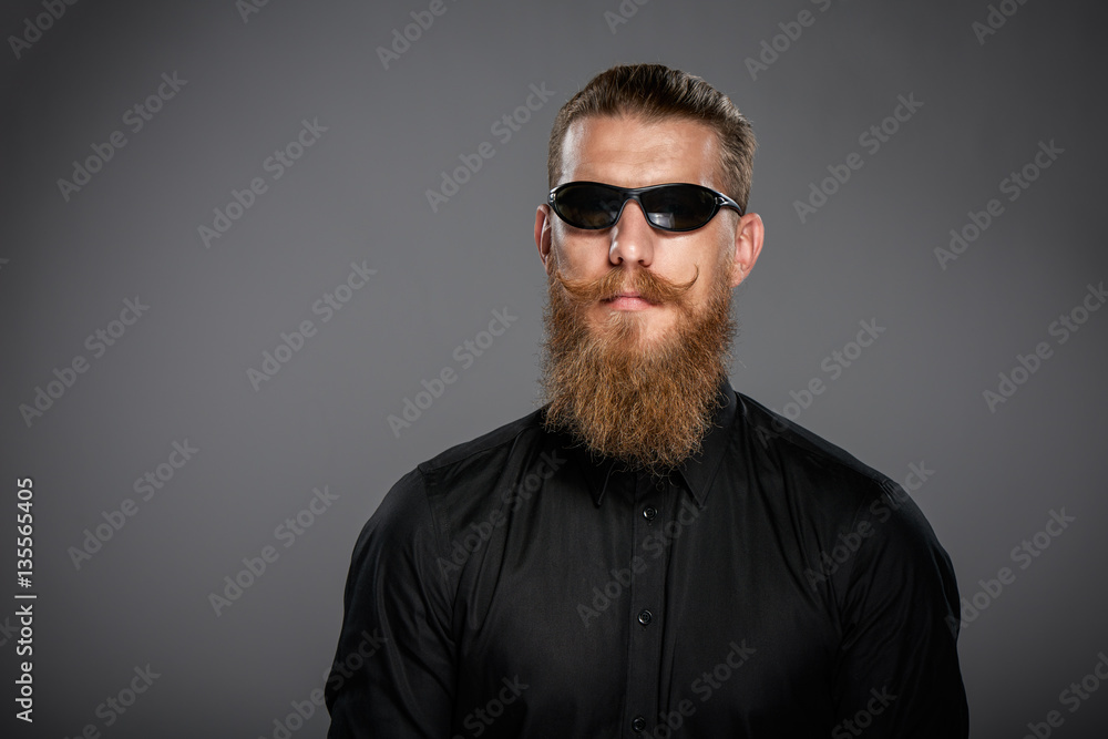 Closeup of hipster man with beard and mustashes wearing black sunglasses, over grey background Closeup of hipster man with beard and mustashes wearing black sunglasses, over grey background