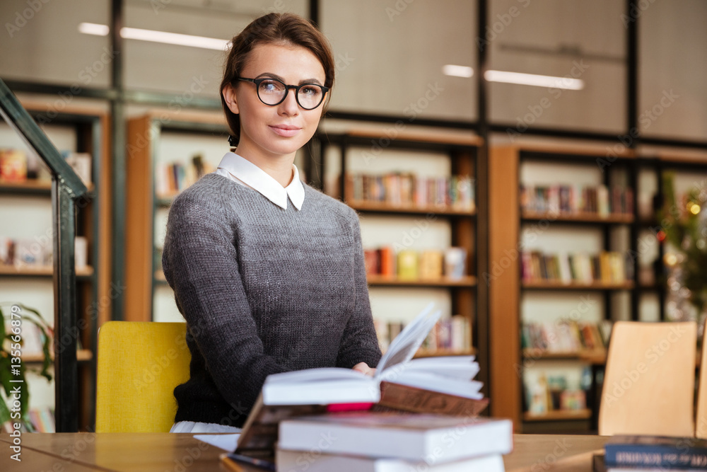 Smiling attractive female student sitting at desk in university library Smiling attractive female student sitting at desk in university library