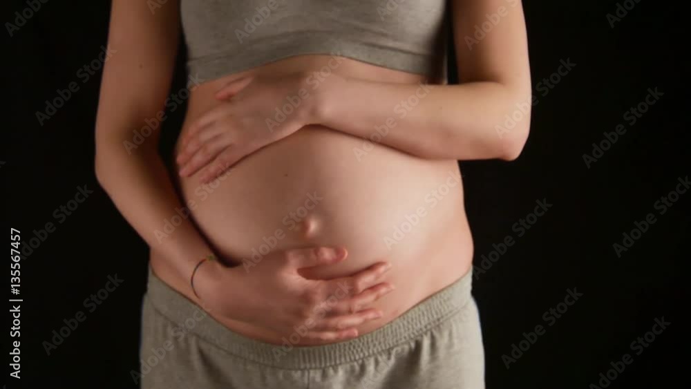 Pregnant woman caressing her tummy on black background Pregnant woman caressing her tummy on black background