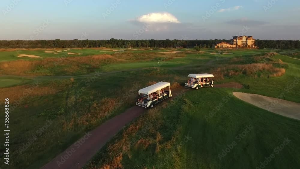 Aerial View of two golf carts with people ride on a golf course on the sunset Aerial View of two golf carts with people ride on a golf course on the sunset
