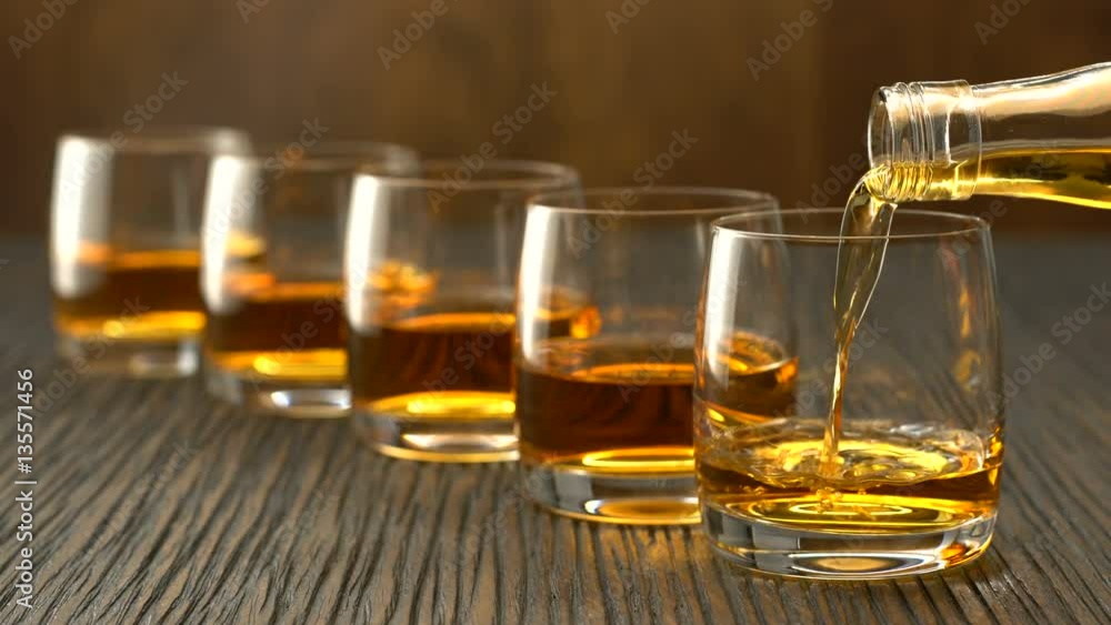 Pouring whiskey into the glass on a wooden table Pouring whiskey into the glass on a wooden table