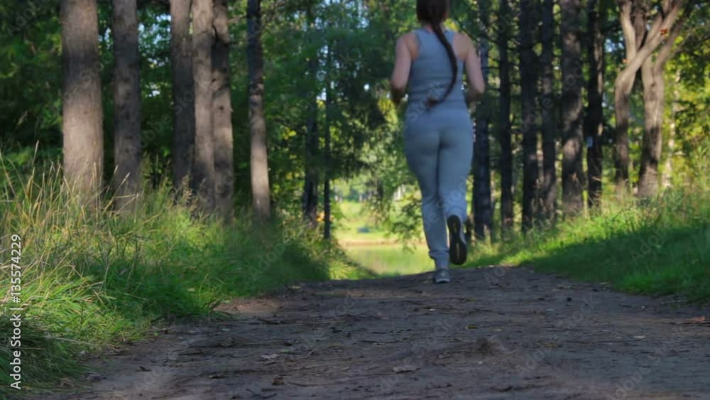Girl runs along a shady forest green alley. Young woman jogging in the park Girl runs along a shady forest green alley. Young woman jogging in the park