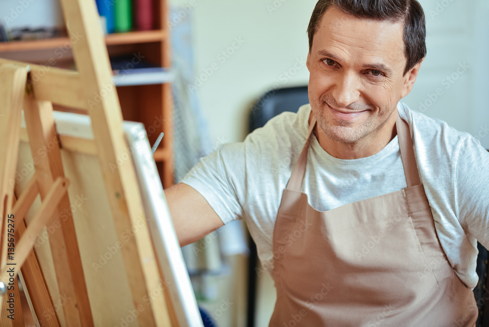Fototapeta premium Satisfied artist posing in painting studio