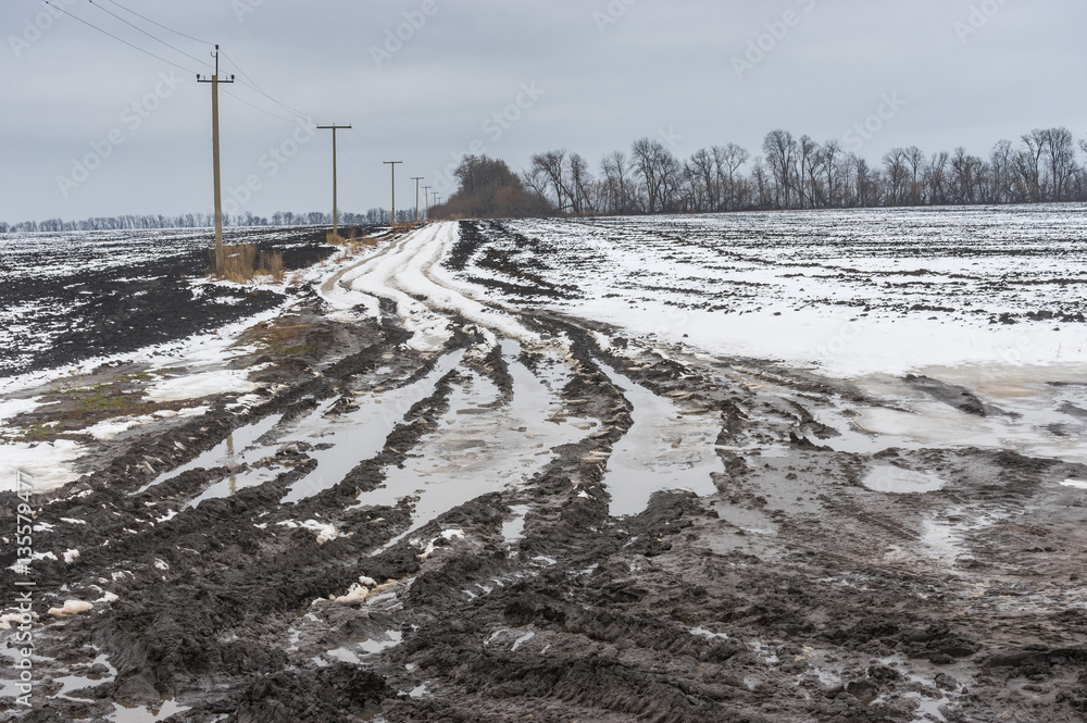 Landscape with dirty country road between agricultural fields in central Ukraine at gloomy winter day