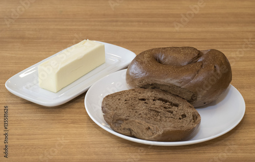 Photography Pumpernickel bagel on white plate and stick of butter on white butter dish on br