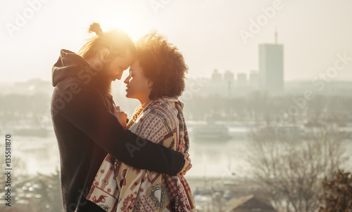 Romantic embracing loving couple enjoying the sunset in front of the city panorama. Falling in love