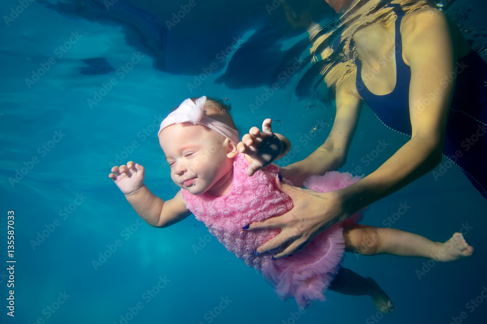Baby in a beautiful dress swims underwater in the pool with my eyes closed, and my mother supported his hands. Portrait. Close-up. Shooting under water. Landscape orientation