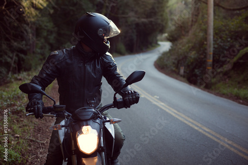 Male astride motorbike on road, looking over shoulder 