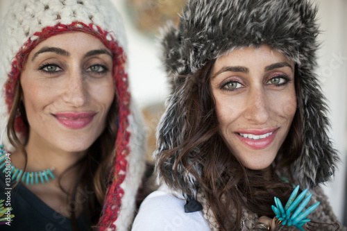 Twin adult sisters wearing winter hats with ear flaps, facing camera 