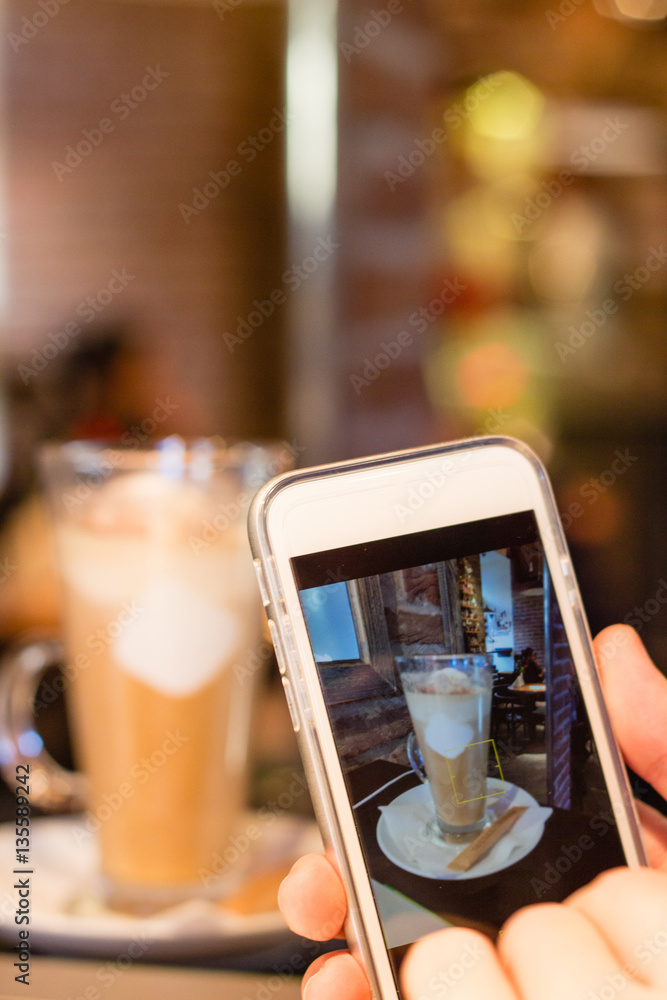 Taking picture of latte coffee with smartphone in cafe