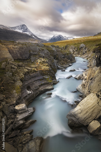 Wonderful sun lit autumn landscape with wild river raging down