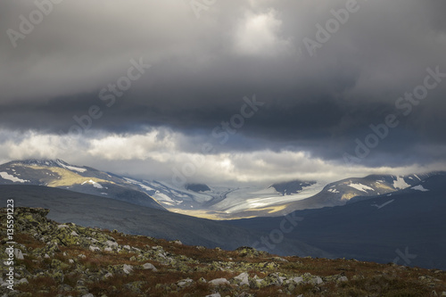 Ancient glaciers landscape in sunlight under stormy and dramatic sky
