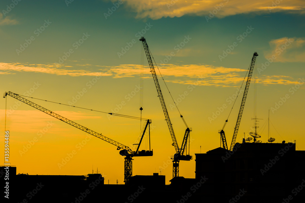 Silhouette of the tower crane on the construction site with city