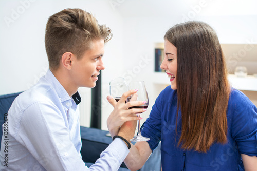 Beautiful young couple with glasses of red wine at home.