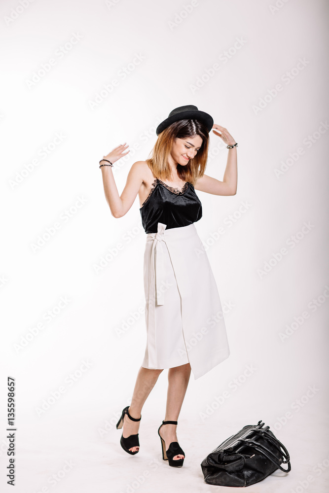 Portrait of girl in Studio in full growth. Black blouse, white skirt, black hat on his head, a beautiful smile. Black bag in his hands. Studio light Portrait of girl in Studio in full growth. Black blouse, white skirt, black hat on his head, a beautiful smile. Black bag in his hands. Studio light