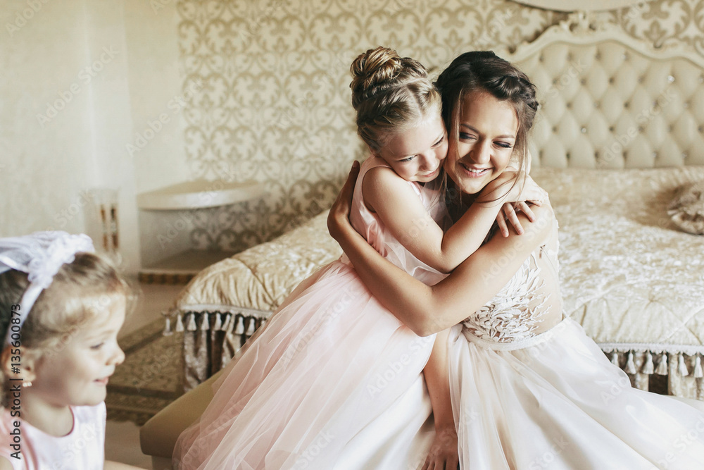 Little girl hugs tender beautiful bride in ivory dress