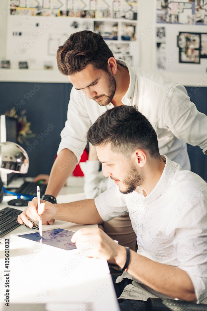 Fototapeta premium Two designer drawing sketches and looking at tablet screen.