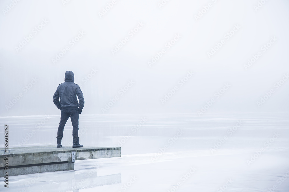 Man in the mist on the lake footbridge in winter afternoon. Peaceful atmosphere. Foggy air. Man in the mist on the lake footbridge in winter afternoon. Peaceful atmosphere. Foggy air.