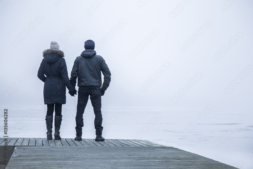 Couple in the mist on the lake footbridge in winter afternoon. Peaceful atmosphere. Foggy air.